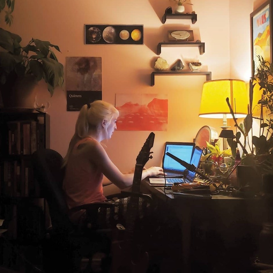 picture of me working at my desk in my millenial-pink room, surrounded by the objects that best capture who I am